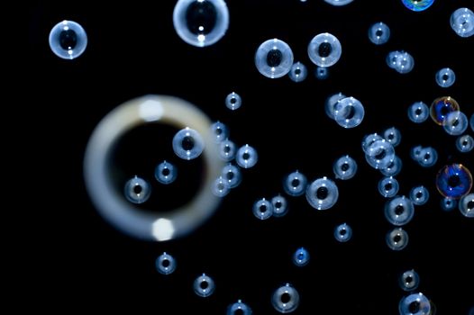 Scattered multiple irridescent blue bubbles in a dark blue-black background