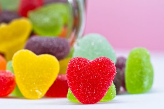 close up view of a redlove-shaped jelly spilled from a glass container on pink background