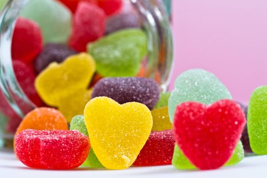 close up view of a yellow love-shaped jelly spilled from a glass container on pink background