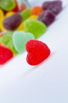 close up view of a redlove-shaped jelly spilled from a glass container on white surface in slanting view