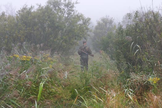 The hunter goes on a footpath in the foggy morning