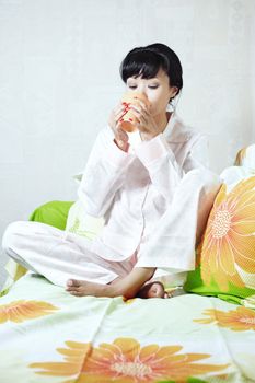 Brunette indoors drinking on a sofa in domestic pijamas