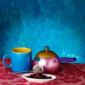 Teapot, cup and herbs on blue background