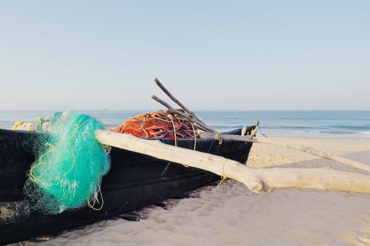 Old boat with fishing net on sandy beach. In Goa