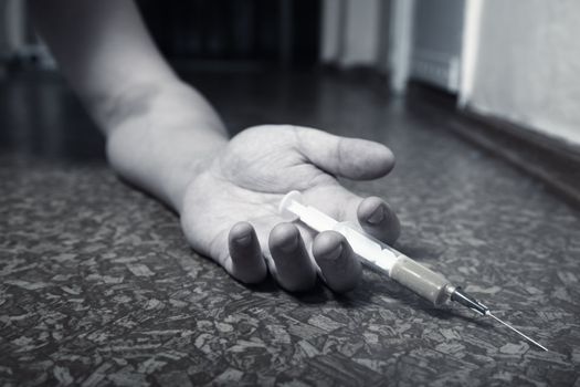 Hand of the narcotist with syringe on the floor. Monochrome photo