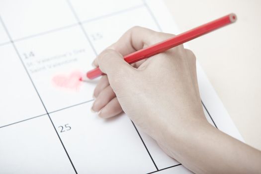 Woman hand drawing heart shape on a calendar