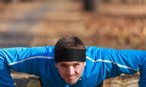 Portrait of a young man doing push-up outdoors in a park in autumn.