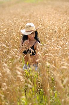 Country Girl In Wheatfield. Sexy young girl in a straw hat standing waist high in a field of ripe wheat.
