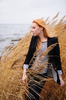 Windswept Lonely Woman. Attractive lonely redhead woman standing on a windswept coastline amongst grasses and reeds staring out to sea.