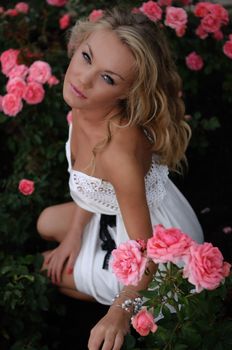 Overhead portrait of a beautiful blonde woman sitting in a bed of pink roses and looking up at the camera.