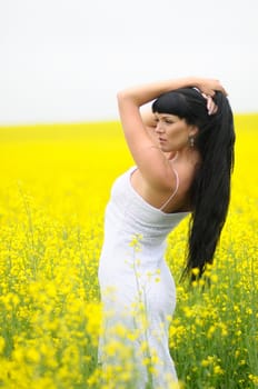 Classic beauty wearing a white dress standing in a field of yellow wildflowers.