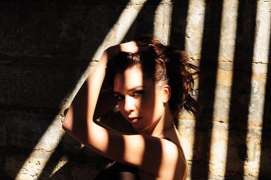 Attractive brunette woman standing in dramatic striped shadows with her hand holding up her tousled hair