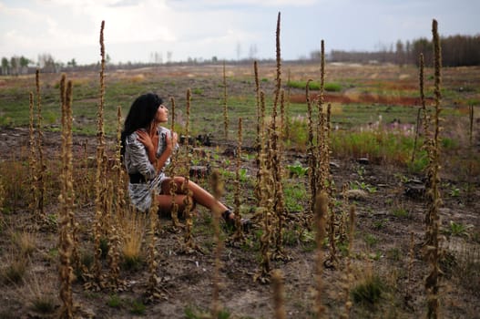 Solitude And Peace. A young woman sits in a vast empty field amongst flower spikes enjoying some solitude and peace.