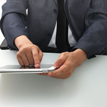 Cropped view of the torso and hands of a man seated at a desk using a tablet computer touching the screen with his finger