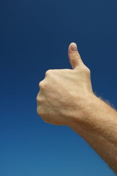 Giving the thumb's up sign against a warm blue sky