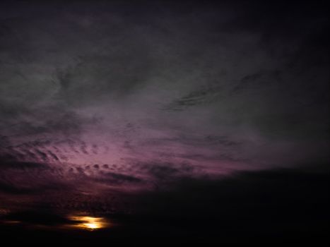 Dark and purplish clouds with the sun shinning at a distance