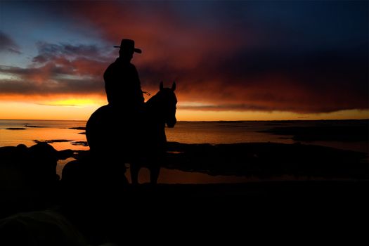 A cowboy on a hill against a sunset and ocean