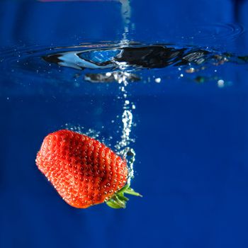 A fresh strawberry dropping in water.