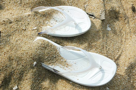 White pair of sandals covered with sand on a beach