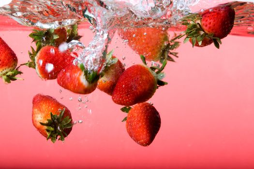 Strawberries falling in red water with splash and bubbles