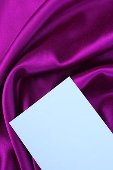 Blank white card on purple and magenta colored satin cloth.