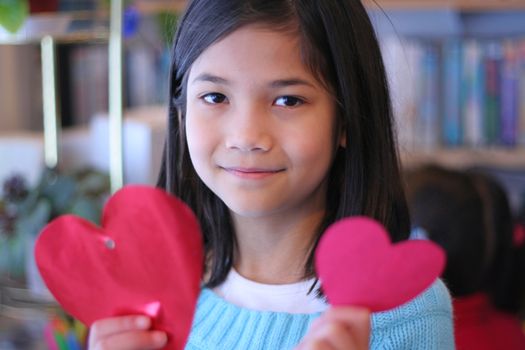 Nine year old girl holding up two red hearts.