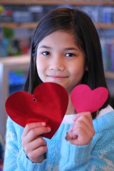 Nine year old girl holding up two red hearts.