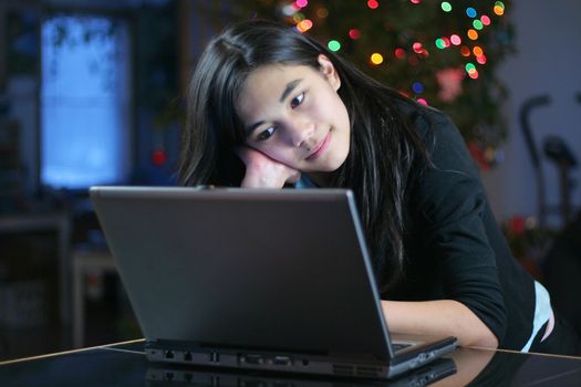 Young teen girl working on the laptop at night.