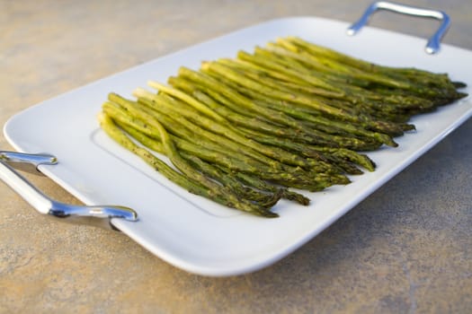 Cooked asparagus on a white square plate on concrete countertop.