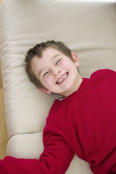 A 6 years old lying on the cushions and smiling large while his eyes squized.