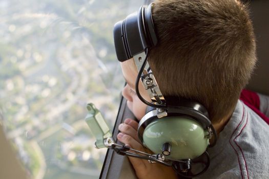 A kid looking down to earth from a small airplane with his headset on.  His reflection on the earth.