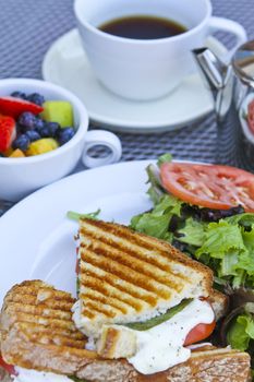 Panini breakfast with complimenting fruits and tea on white plates.