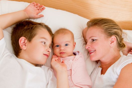 Mother and her kids in the bed, big brother and mother looking at  newborn swaddled newborn.