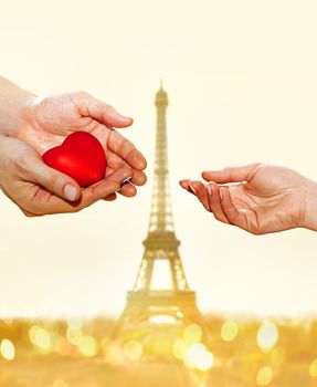 artificial red heart on hands of man for woman on Eiffel Tower background