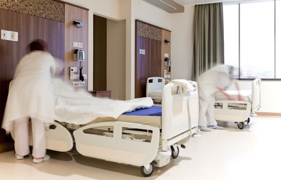 Blurred images of staff members changing hospital bed sheets in modern equipped room