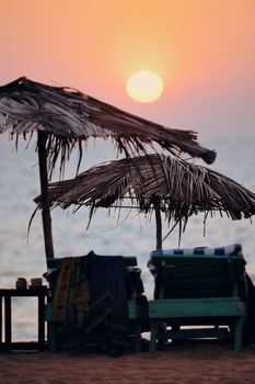 Exotic lean-to of palm leaves and deck chairs in sunset