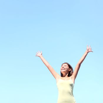 Freedom concept. Free woman smiling happy with arms raised joyful under clear blue sky. Beautiful young multiracial Asian / Caucasian girl in her 20s.