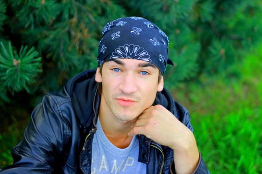A handsome man in a bandana and a leather jacket in black, looks at you with piercing blue eyes