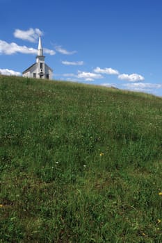 Photo of a little white wooden church on the top of a hill.