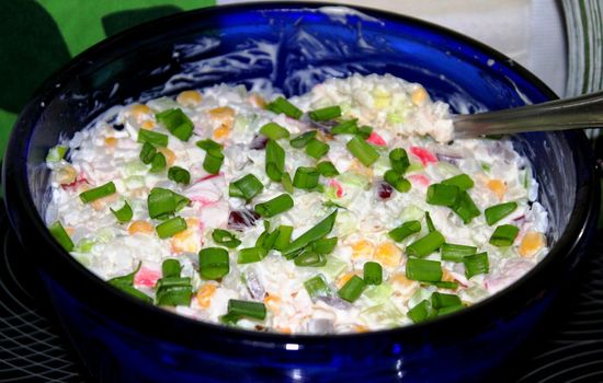 Crab Salad in Russian recipe in a blue bowl, sprinkled with green onions