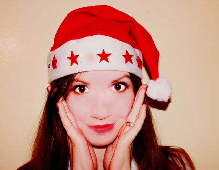 Portrait of happy girl in a Christmas hat. She is smiling and holding hands in the face