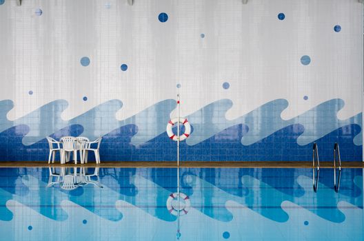 White plastic table and chairs, safety ring, ladder at pool side and reflect in water