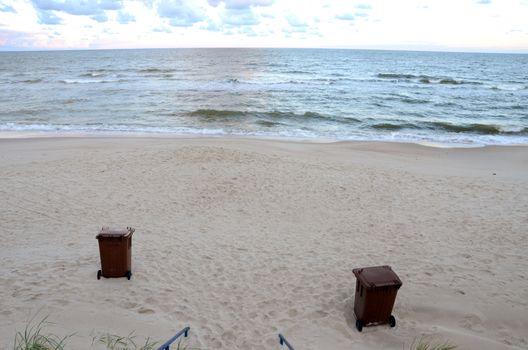 Garbage containers in sea sand. Sea waves. Natural seashore backdrop.