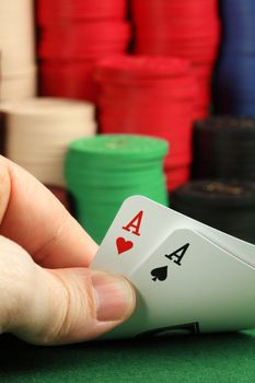 Photo of a card player holding two aces in focus, and a stack of gambling chips blurry in the background.