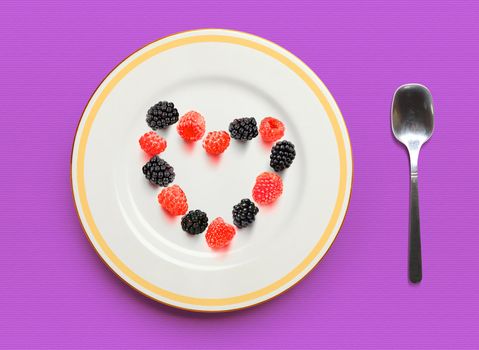 Heart from raspberry and blackberry on white plate