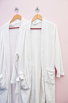 Two white bathrobes hanging on the wall