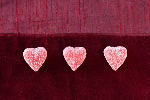 Three jelly (gummy) sugar coated candy hearts in a row on red textured background.