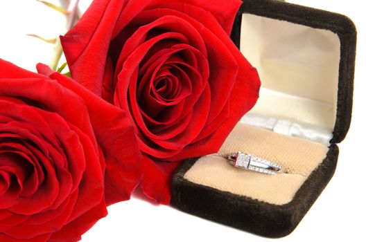 An engagement ring with red roses next to it, isolated against a white background.