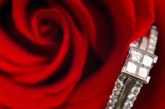 A macro view of a diamond engagement ring, resting in a red rose.