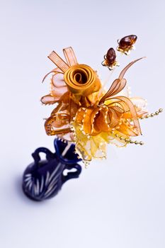Angled view of a brown flower made by ribbon in blue vase on white background in portrait orientation